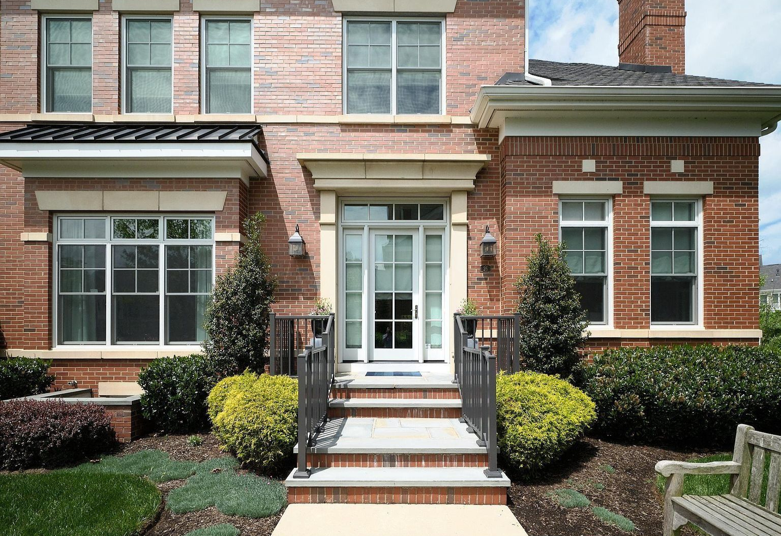 Brick townhouse entrance with white double doors, steps, black railings, and trimmed bushes