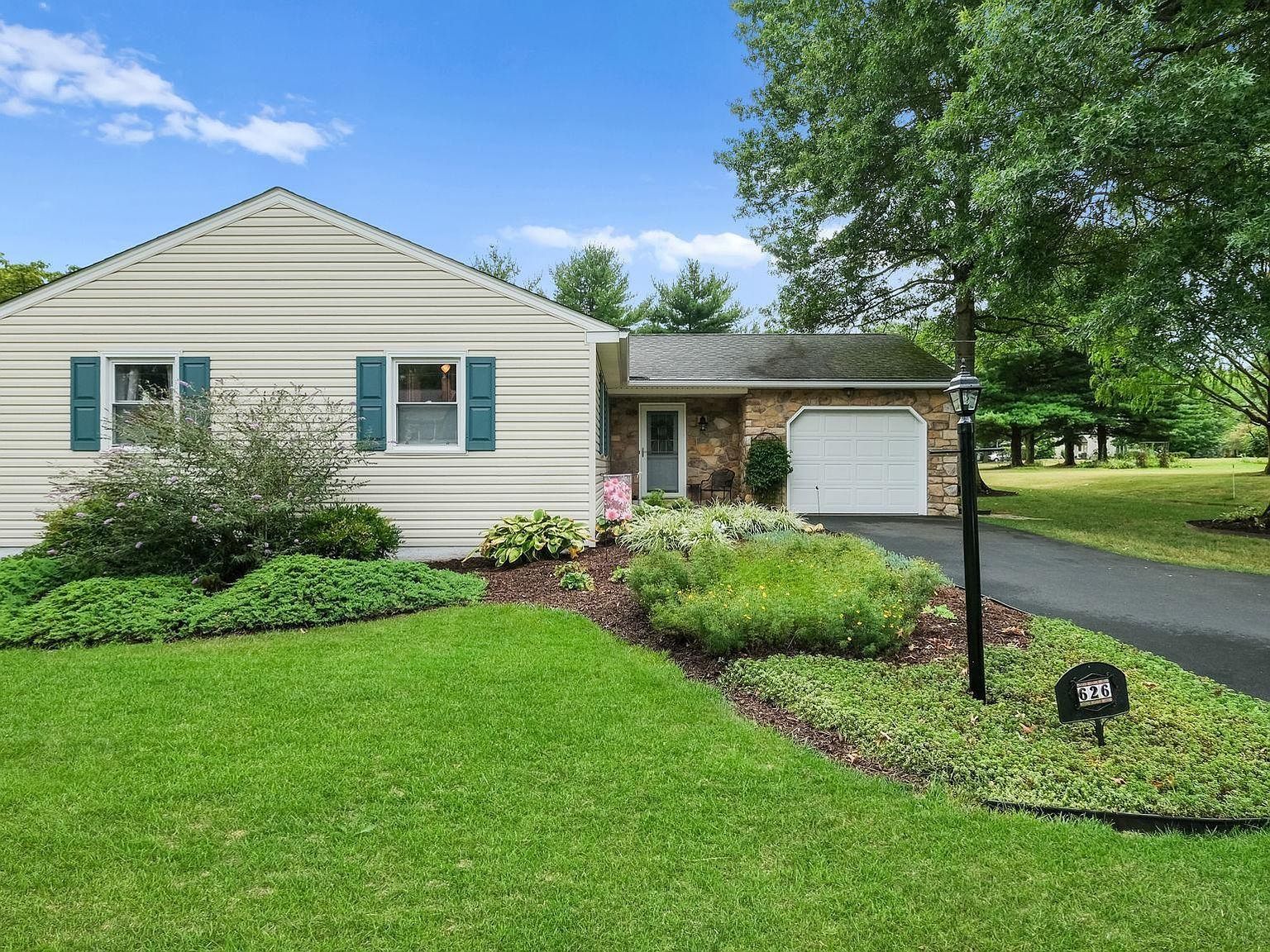Single-story house with white siding, green shutters, garage, and a neatly landscaped front lawn.