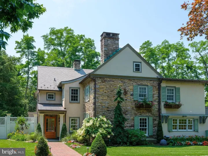 Stone-and-stucco house with green shutters and a chimney, surrounded by trees and landscaping