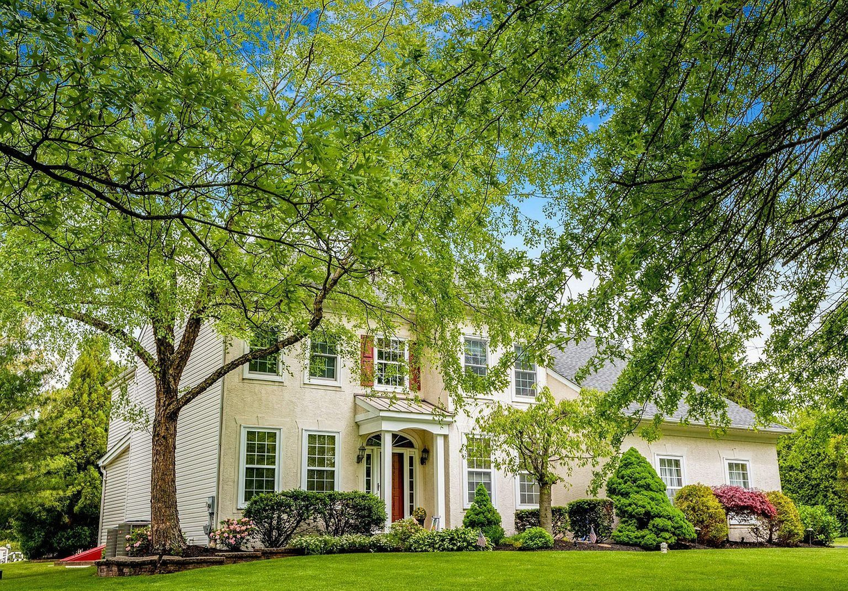 Two-story white house with columns, green shutters, and a lush front lawn under leafy trees