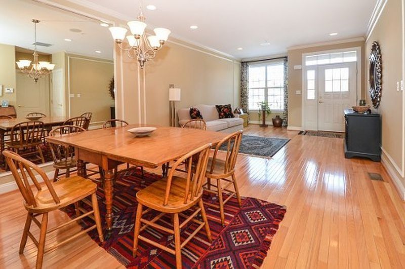 Bright dining room with wooden table, chairs, mirrored wall, hardwood floors, and front entry.
