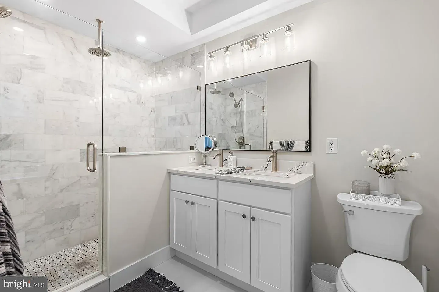 White tiled bathroom with glass shower, vanity with mirror, and toilet