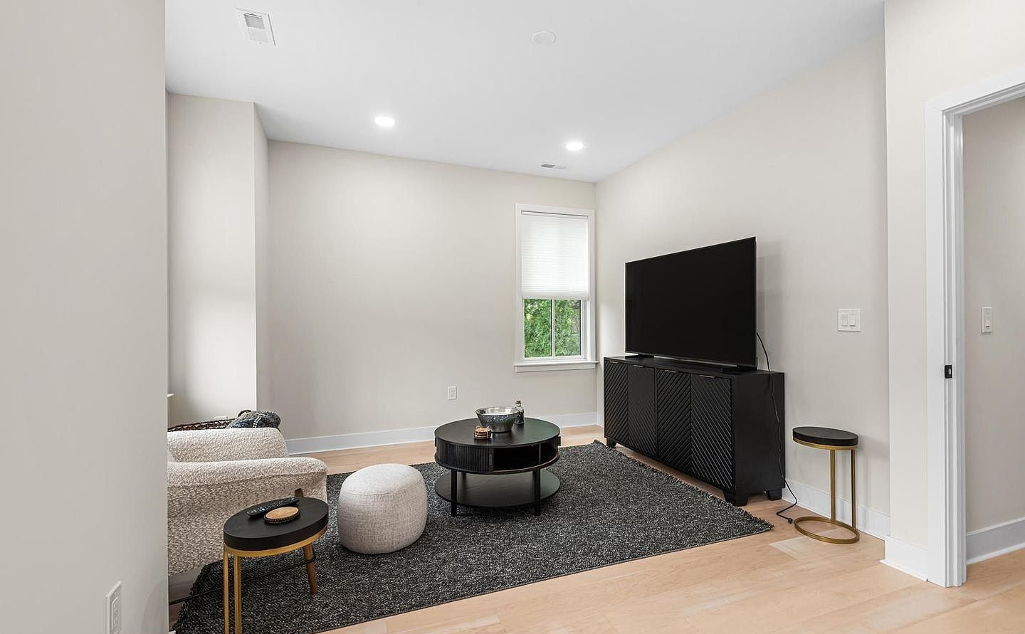 Modern living room with a gray rug, black TV stand, sectional sofa, and a small window.