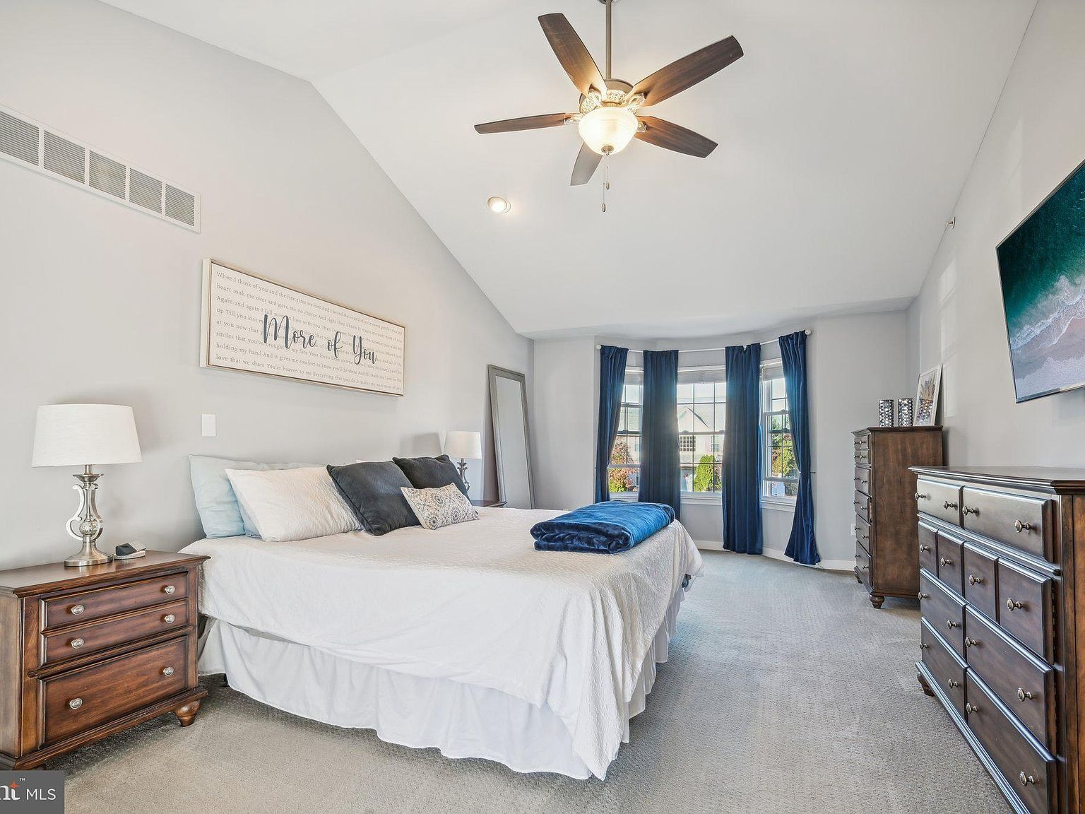 Bright bedroom with white bedding, blue accents, ceiling fan, and French doors leading outside.