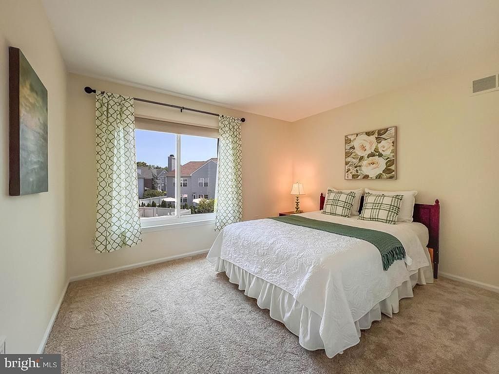 Bright bedroom with a white bed, patterned curtains, and a large window overlooking homes outside