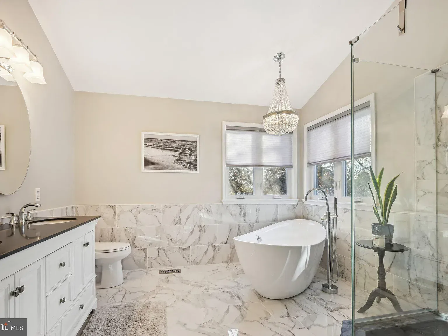 Bright modern bathroom with freestanding tub, marble tile, glass shower, and vanity sink.