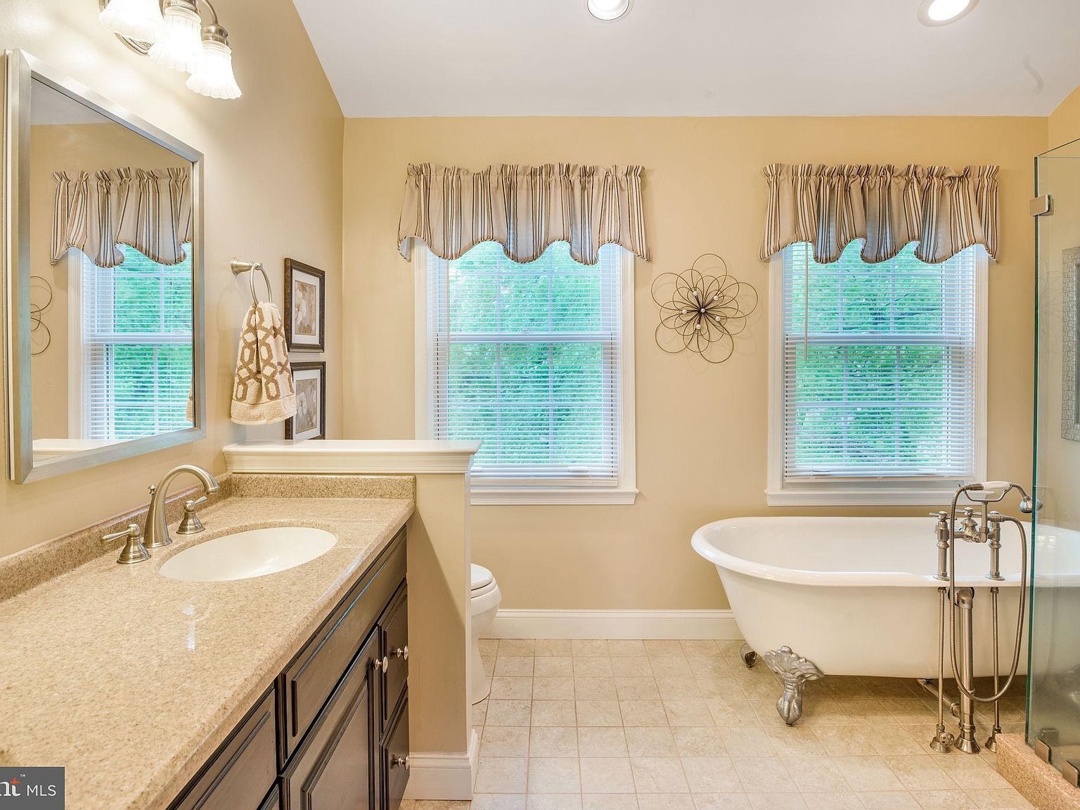 Bright beige bathroom with vanity, two windows, and a white clawfoot tub
