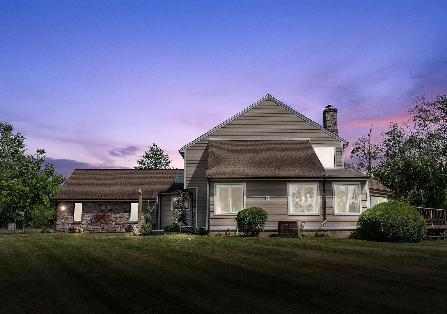 Suburban house with lit windows at dusk under a purple sky