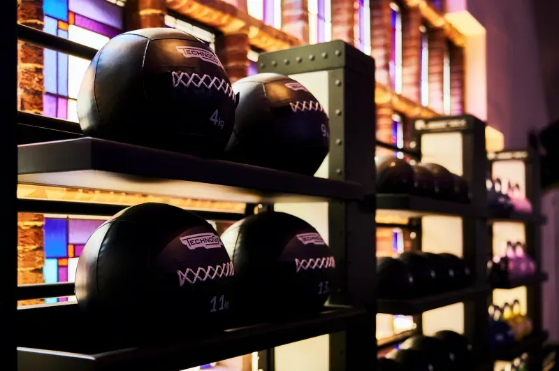 Zwarte medicijnballen opgestapeld op sportschoolrekken, met kleurrijk licht van het raam op de achtergrond
