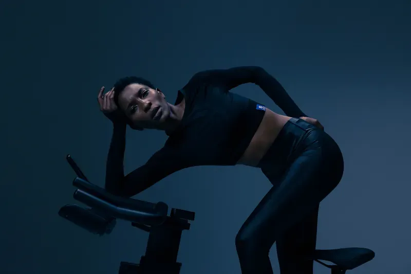 Vrouw in zwarte sportkleding die zich uitrekt op een hometrainer in een donkere studio