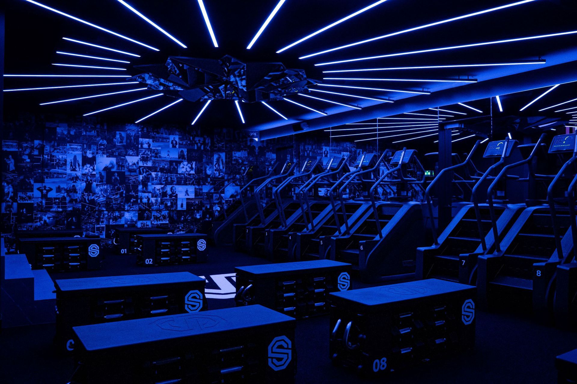 Futuristische zaal in blauw licht, met rijen stoelen en oplichtende plafondlampen