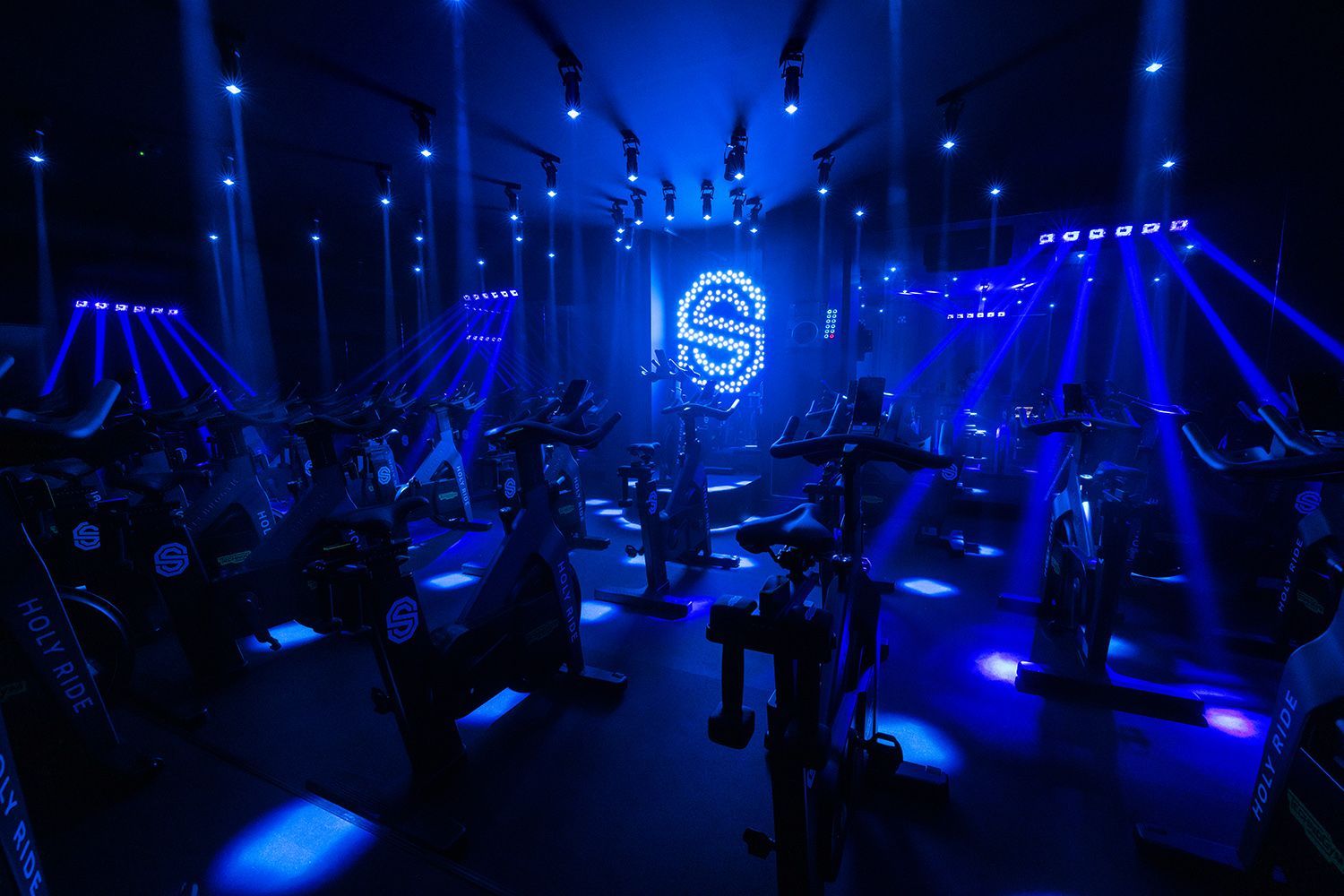 Blauw verlichte sportschool met mensen die trainen op hometrainers onder neonverlichting