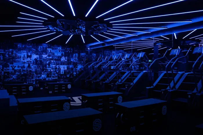 Esportsarena met blauwe verlichting, rijen gamingstoelen en grote podiumlampen aan het plafond