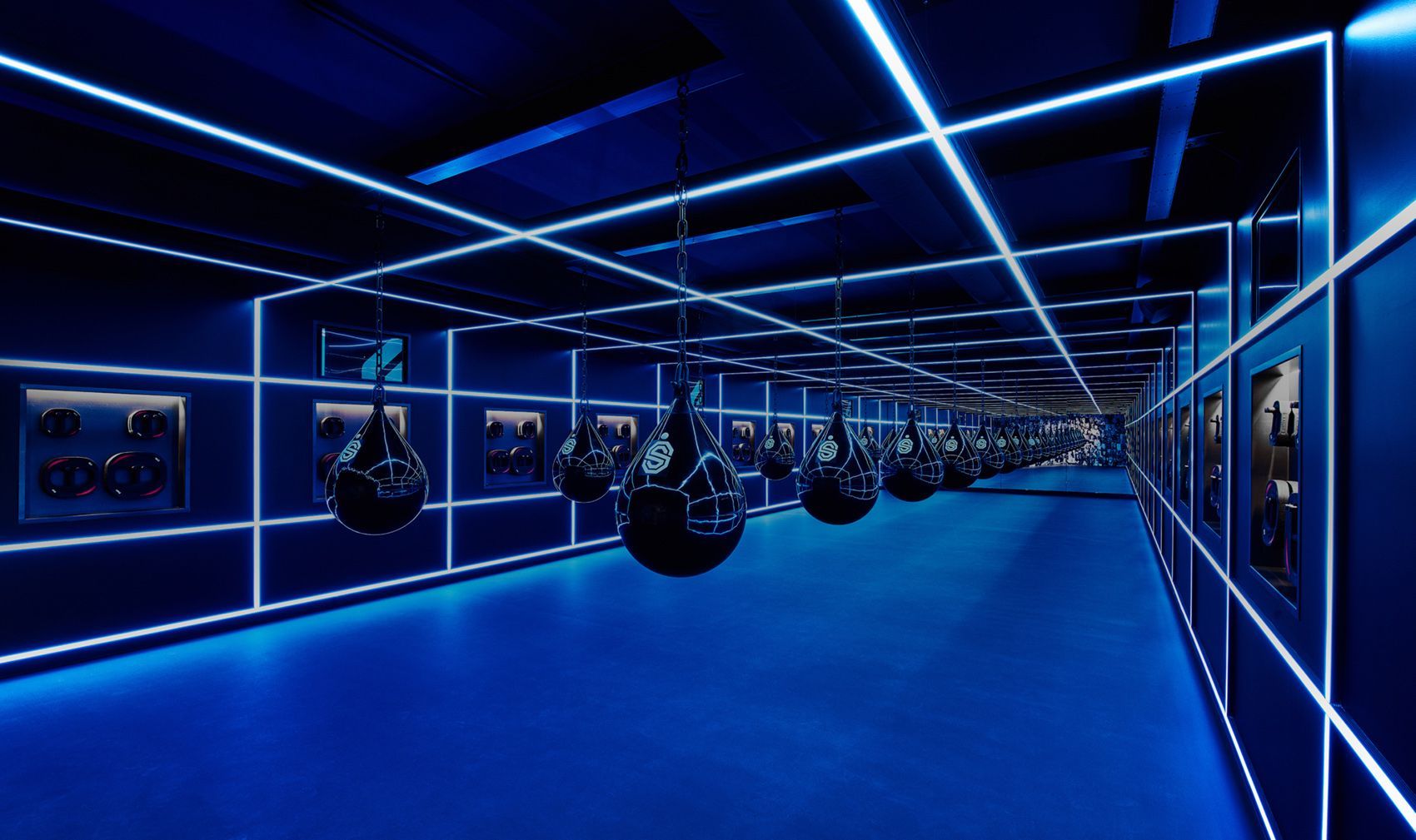 Blauw verlichte binnengang van een sportschool met hangende bokszakken en gloeiende ledstrips
