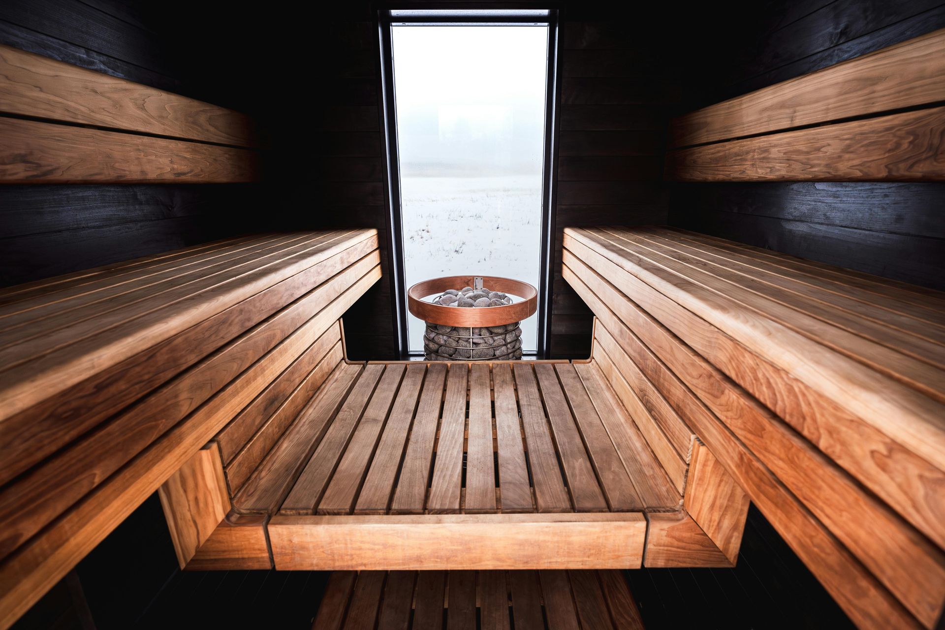 Houten saunabanken met uitzicht op een kleine emmer en een lichte deuropening aan het einde van de ruimte