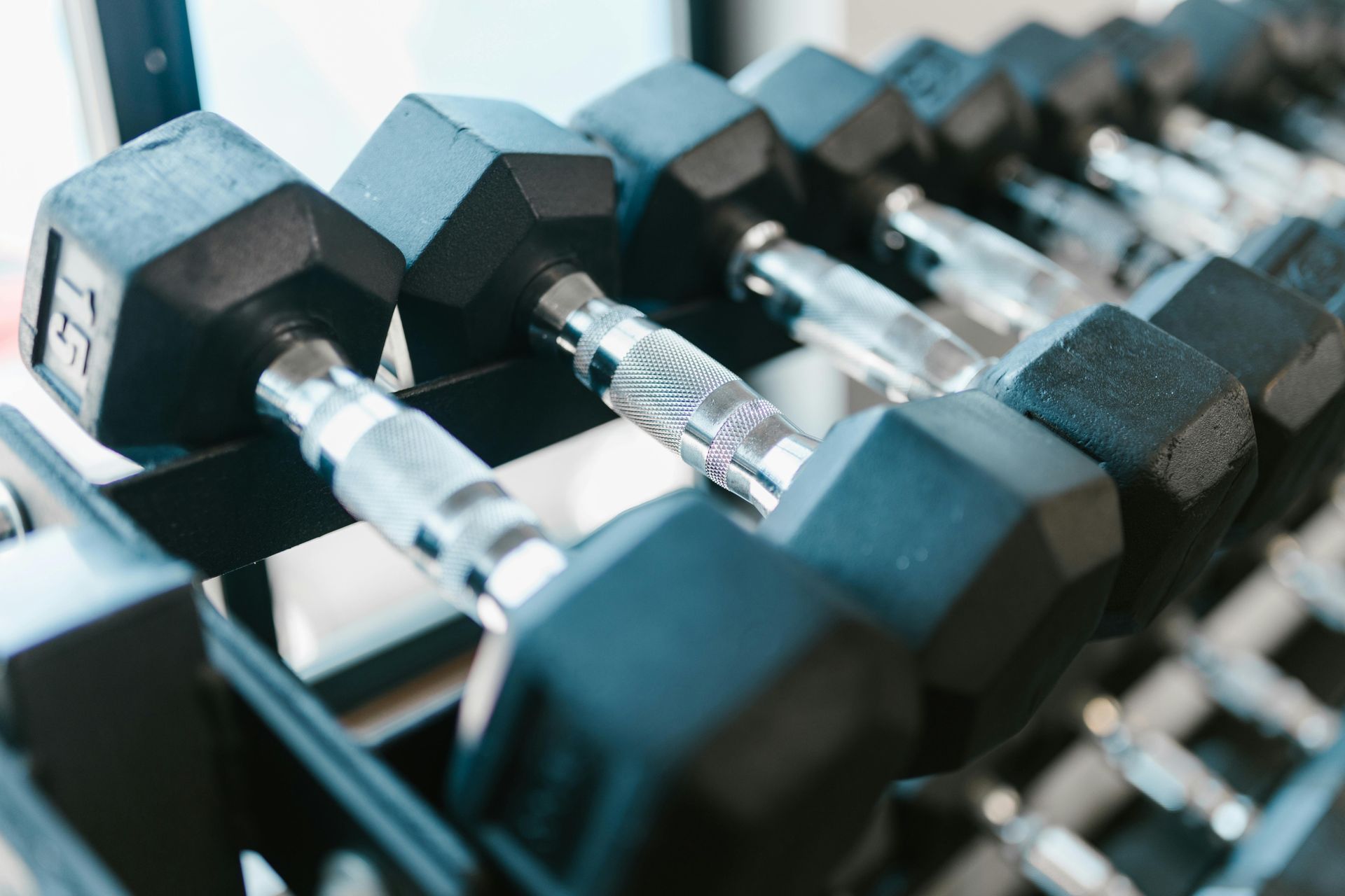 Rij hexagonale dumbbells op een rek, met zwarte en zilveren handgrepen in een sportschool