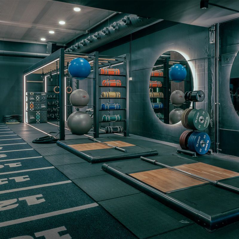 Indoor sportszaal met fitnessballen, spiegels en balansplatforms op een donkere kunstgrasvloer.