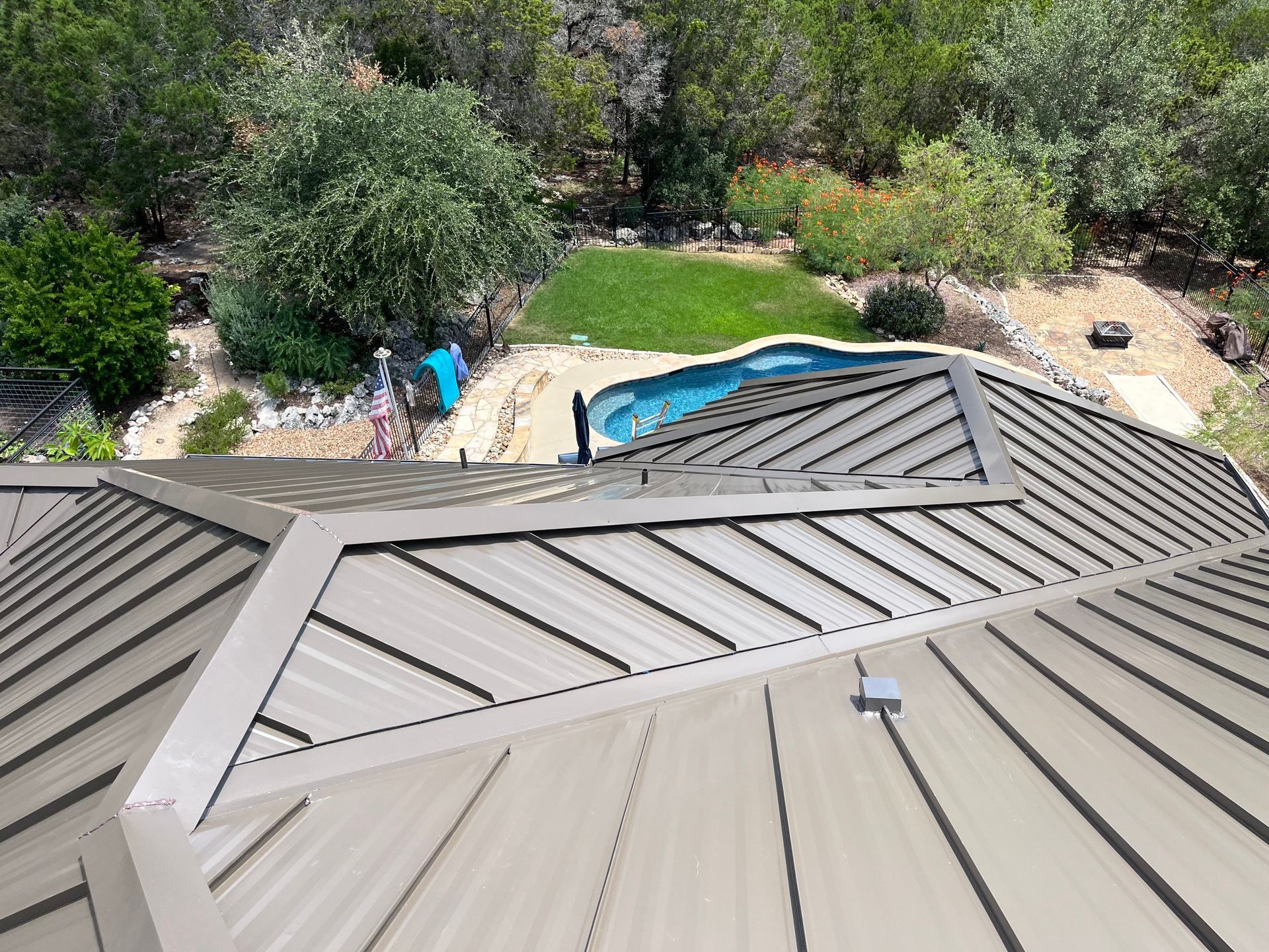 View of a metal roof, overlooking a backyard with a pool and greenery.