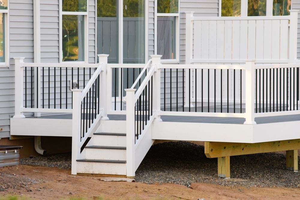 A white deck with black railing and stairs is in front of a house.
