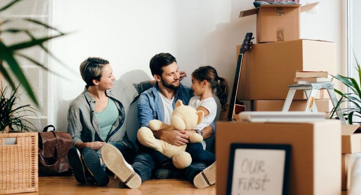 A family is sitting on the floor in their new home surrounded by boxes.