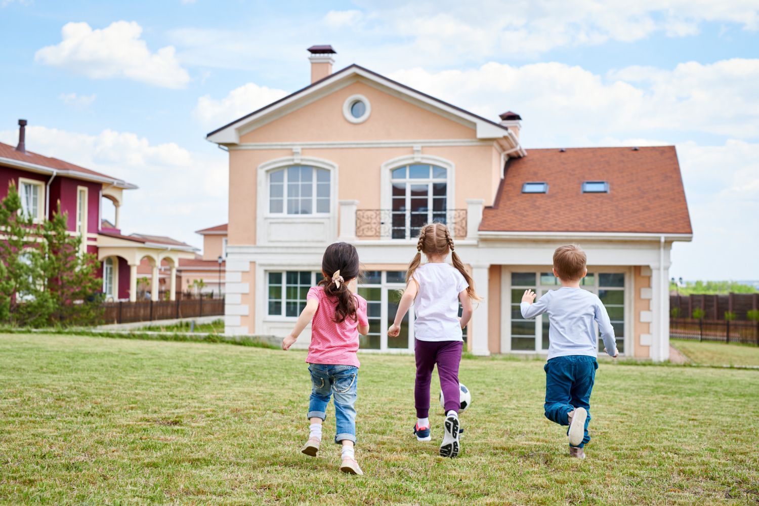 Three children are running in front of a large house.