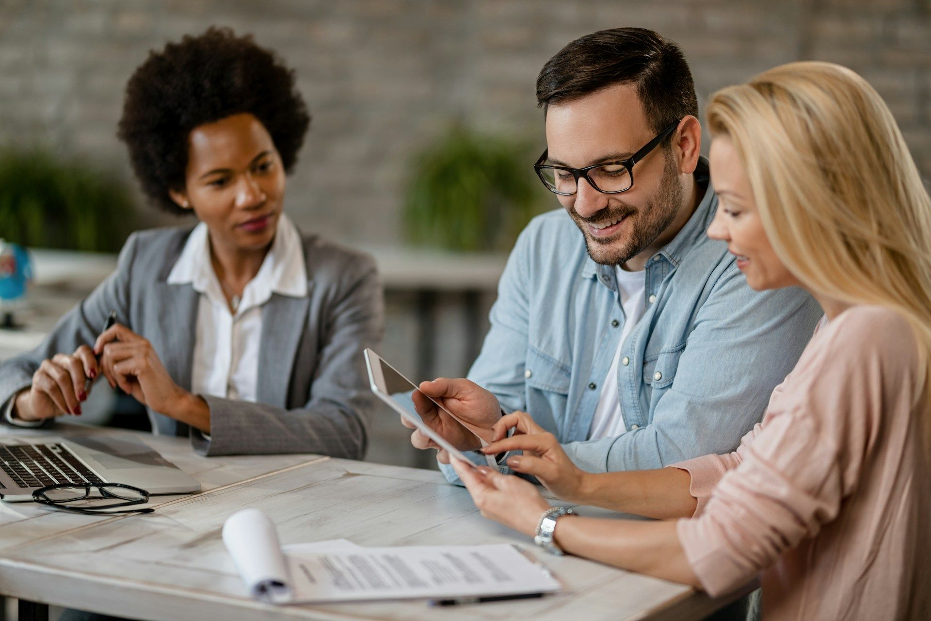A group of people are sitting at a table looking at a tablet.