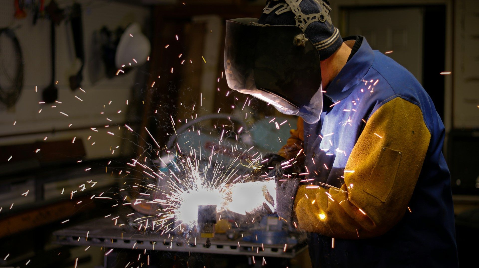A man wearing a welding mask is welding a piece of metal.