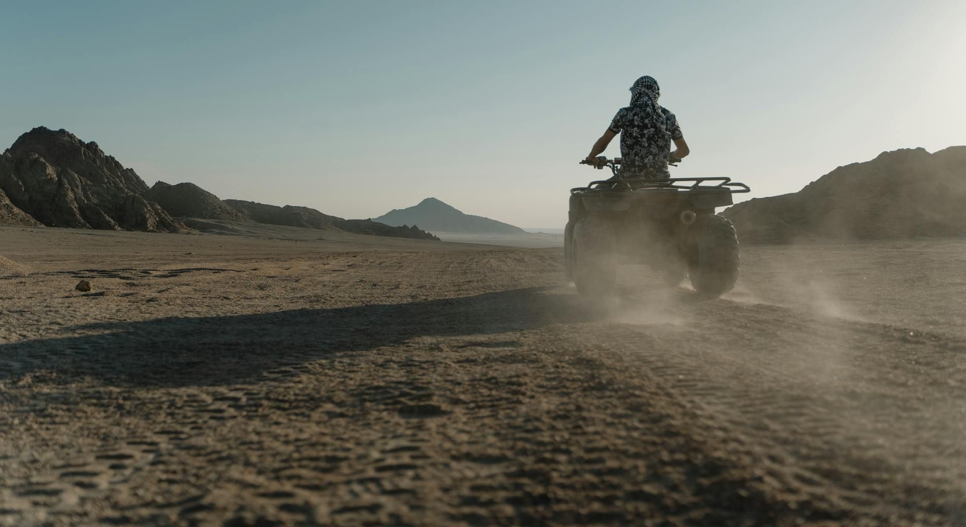 A man is riding an atv on a dirt road in the desert.