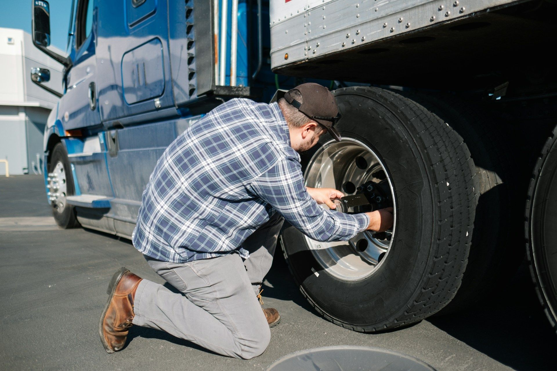 A man is kneeling down to fix a tire on a semi truck.