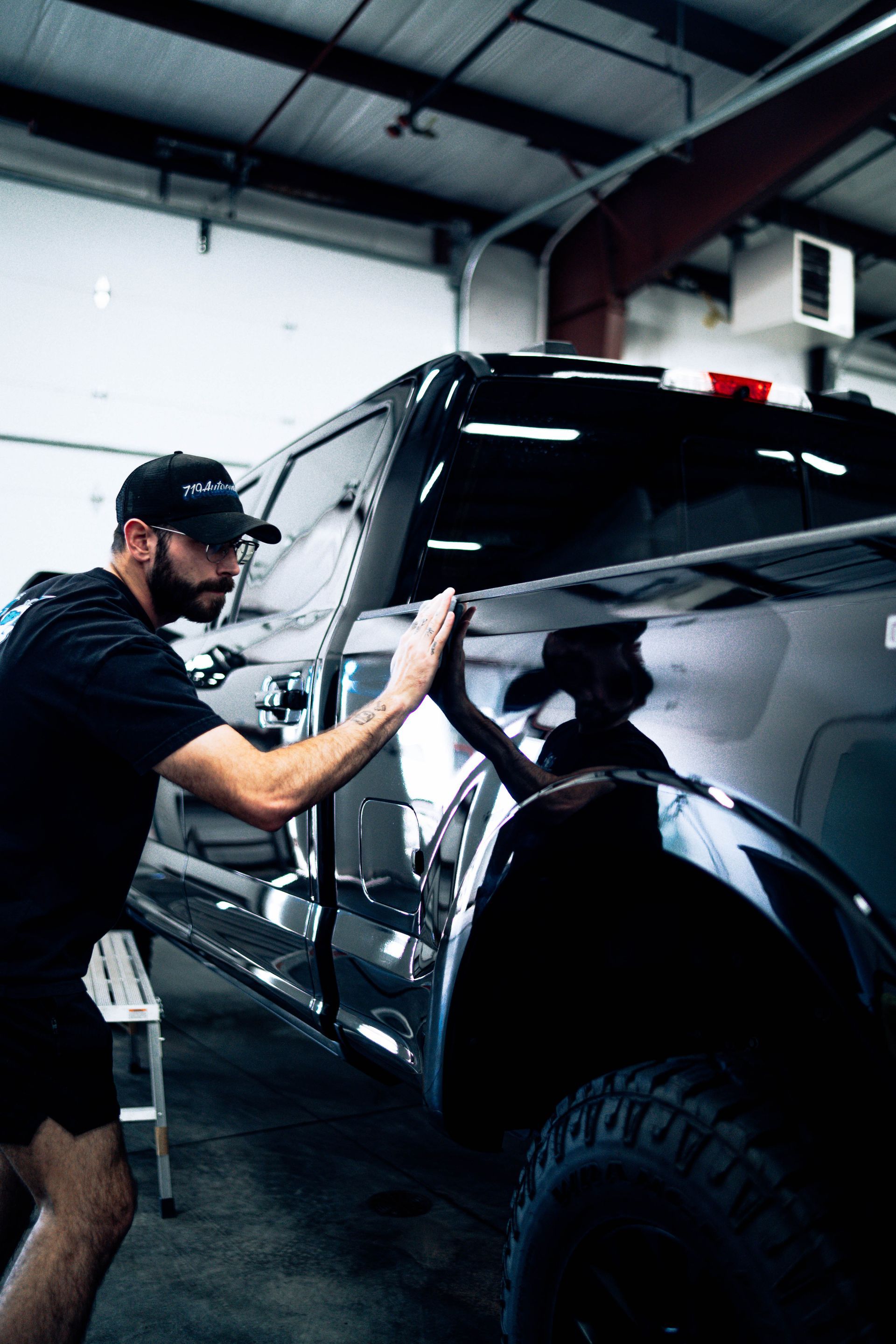 Mechanic polishing a black truck in a garage under bright overhead lights