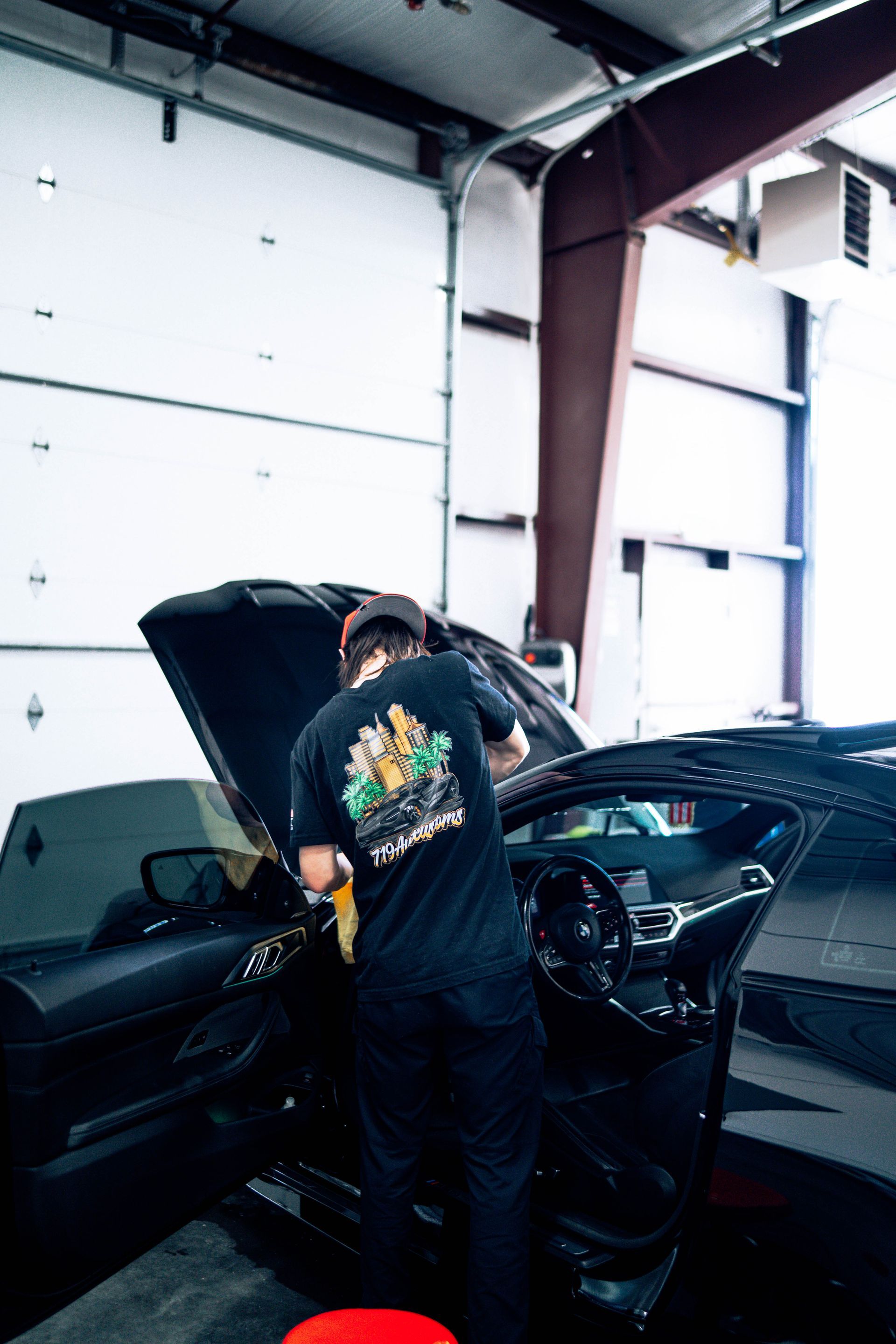 Person working on a black car with the hood open inside a garage