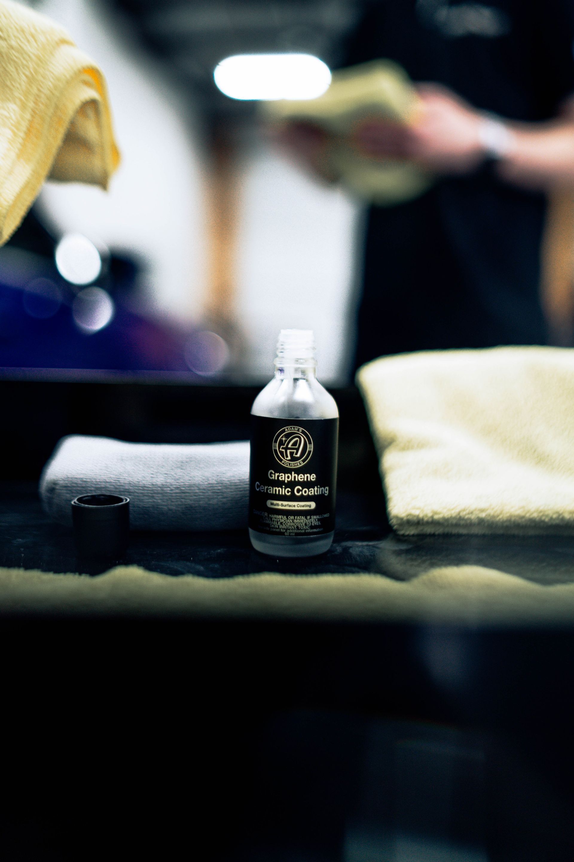 Small black bottle on a dark towel beside folded towels in a softly blurred spa or bathroom setting
