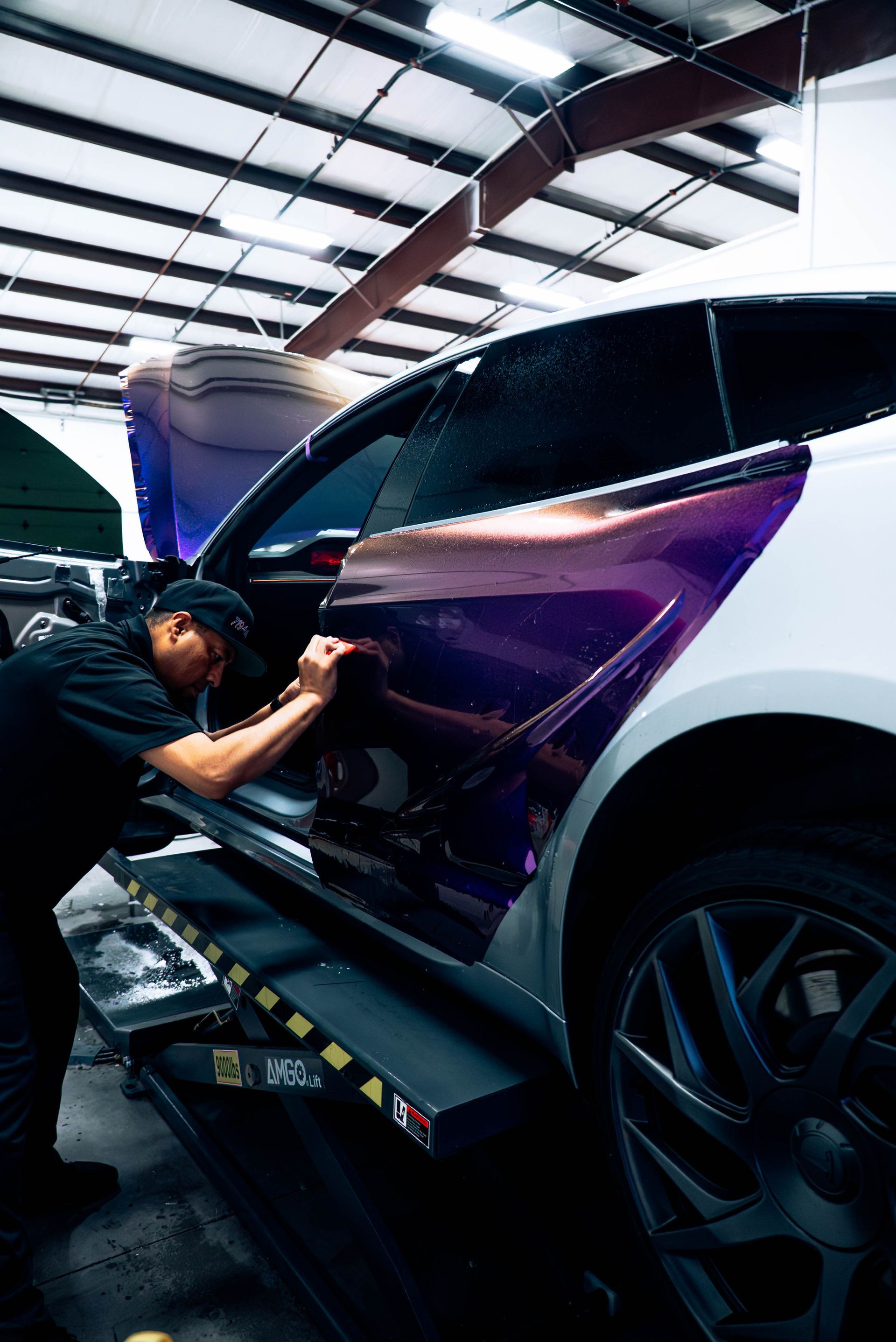 Mechanic polishing the open door of a white car in a garage under bright lights