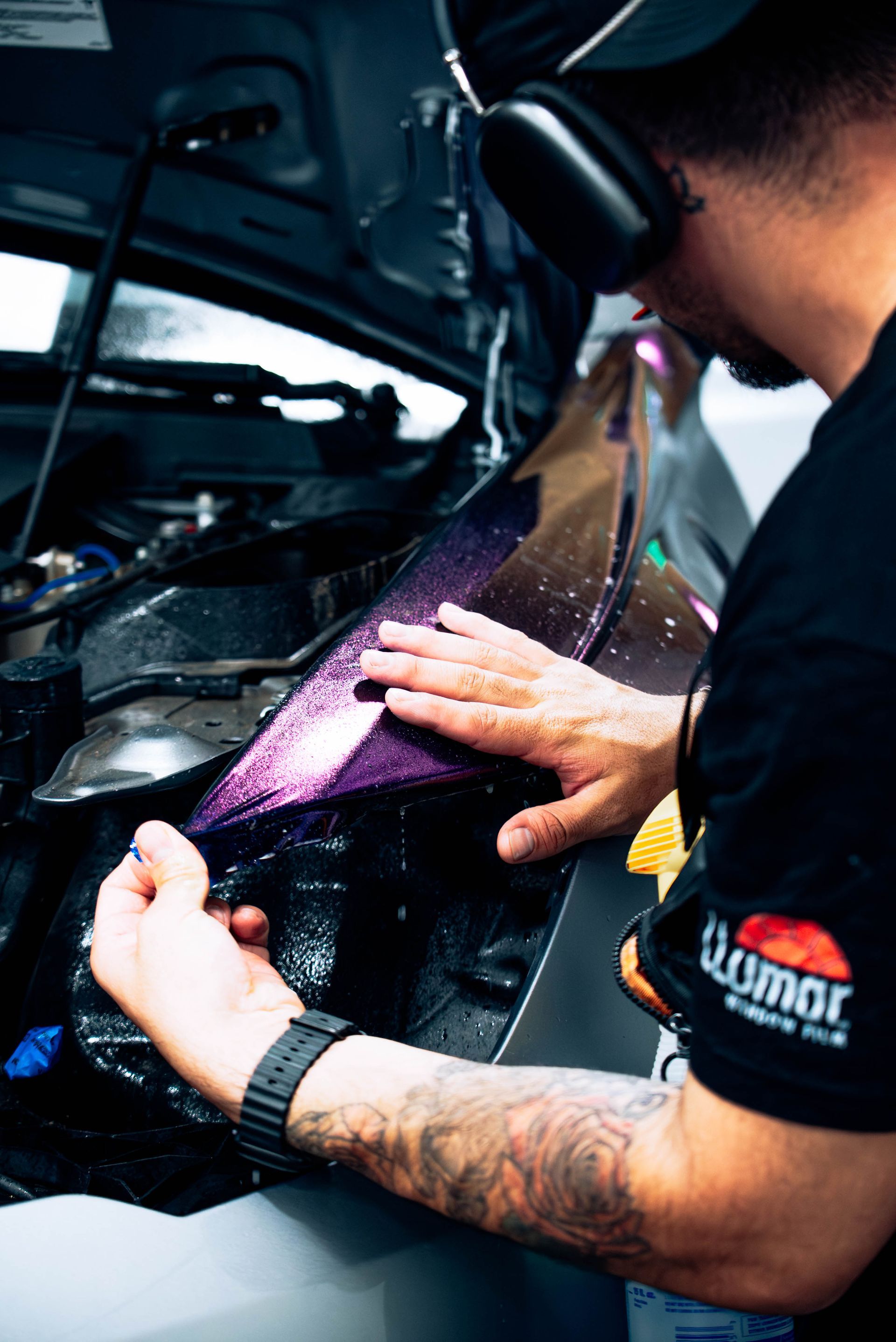 Mechanic polishing a car engine compartment with a cloth, wearing gloves and headphones