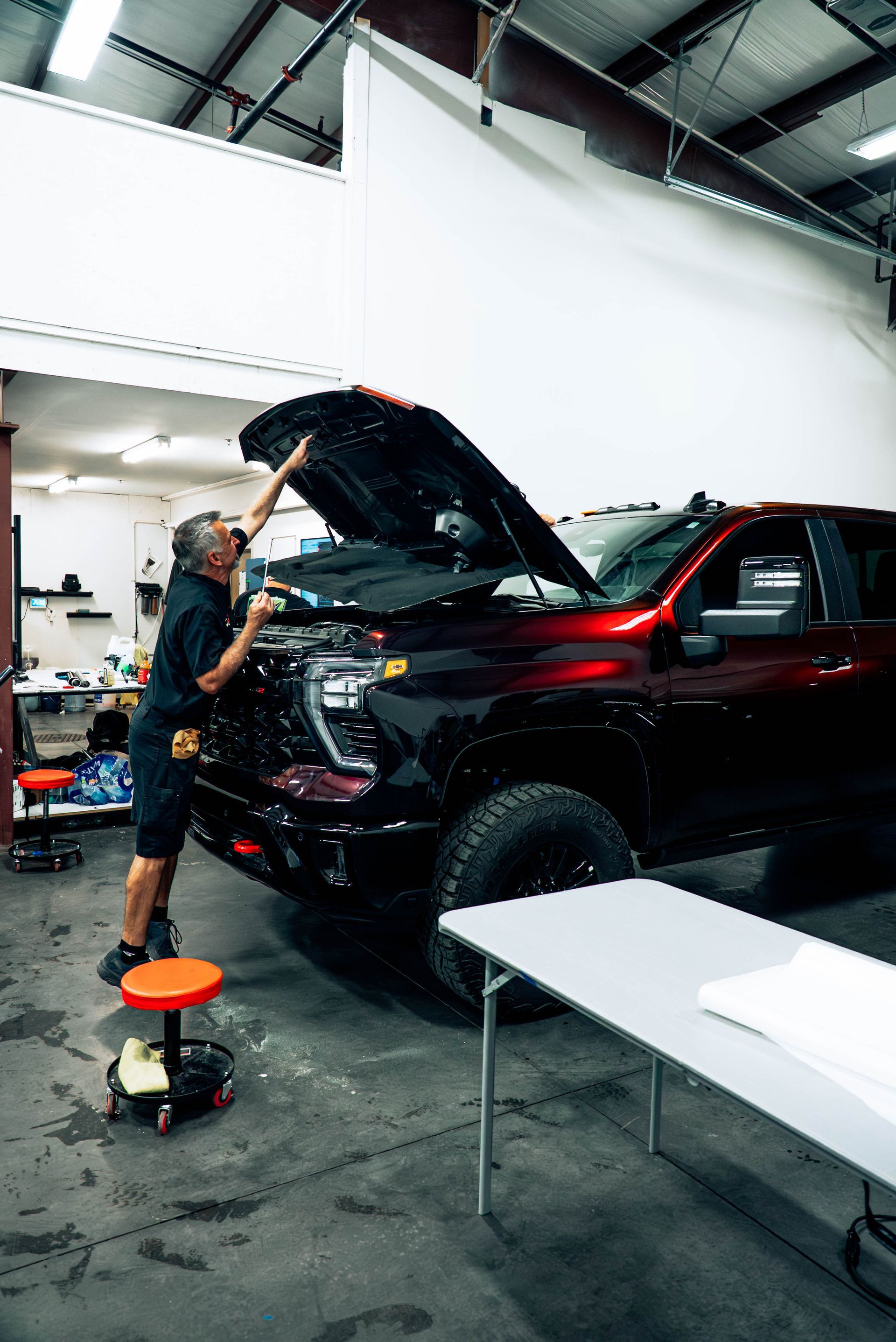 Mechanic working on a black SUV with hood open in a garage workshop