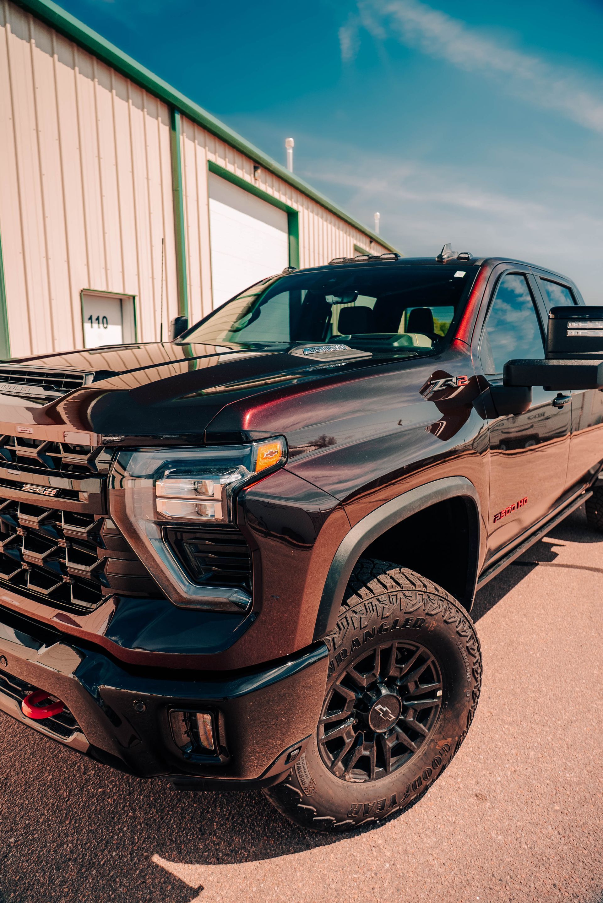Black lifted pickup truck parked beside a warehouse on a sunny day