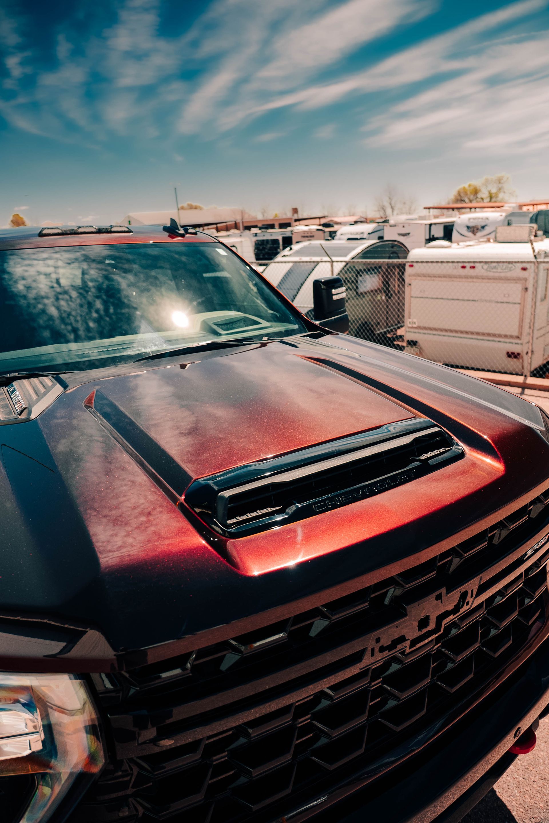 Red pickup truck with black hood scoop parked among white trucks under a bright sky