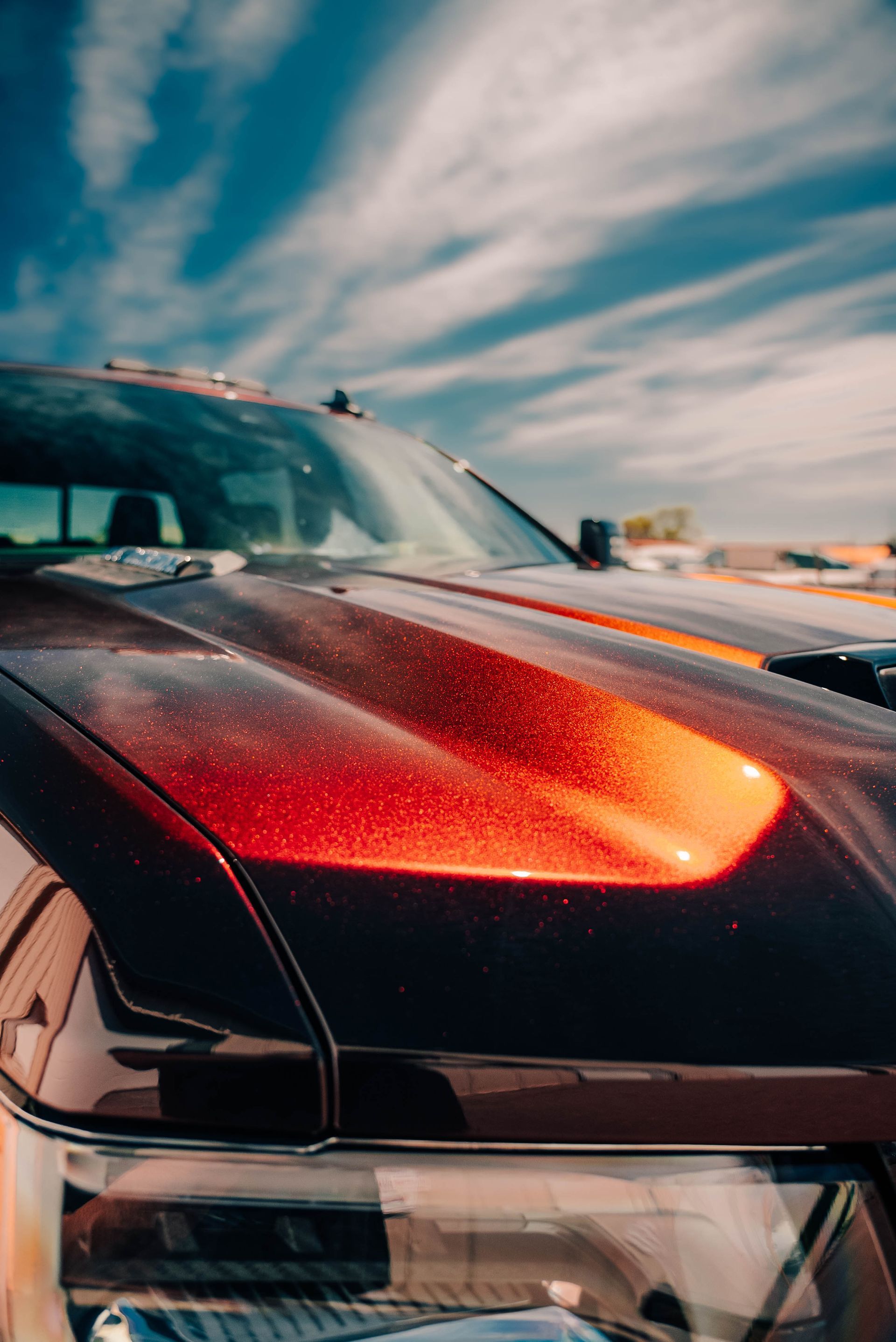 Close-up of a black sports car with a glowing red headlight under a dramatic sky