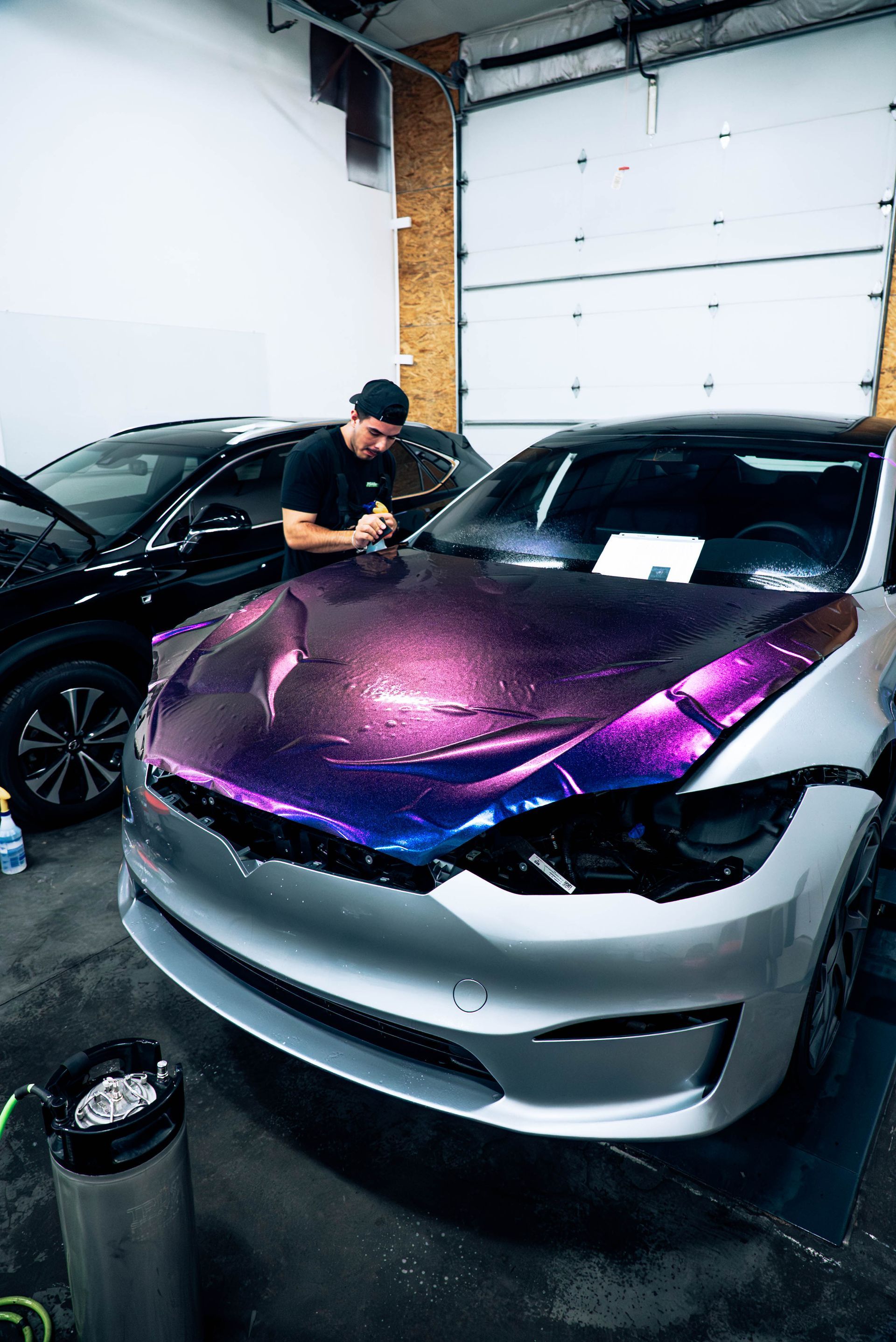 Person applying purple vinyl wrap to a silver car in a garage