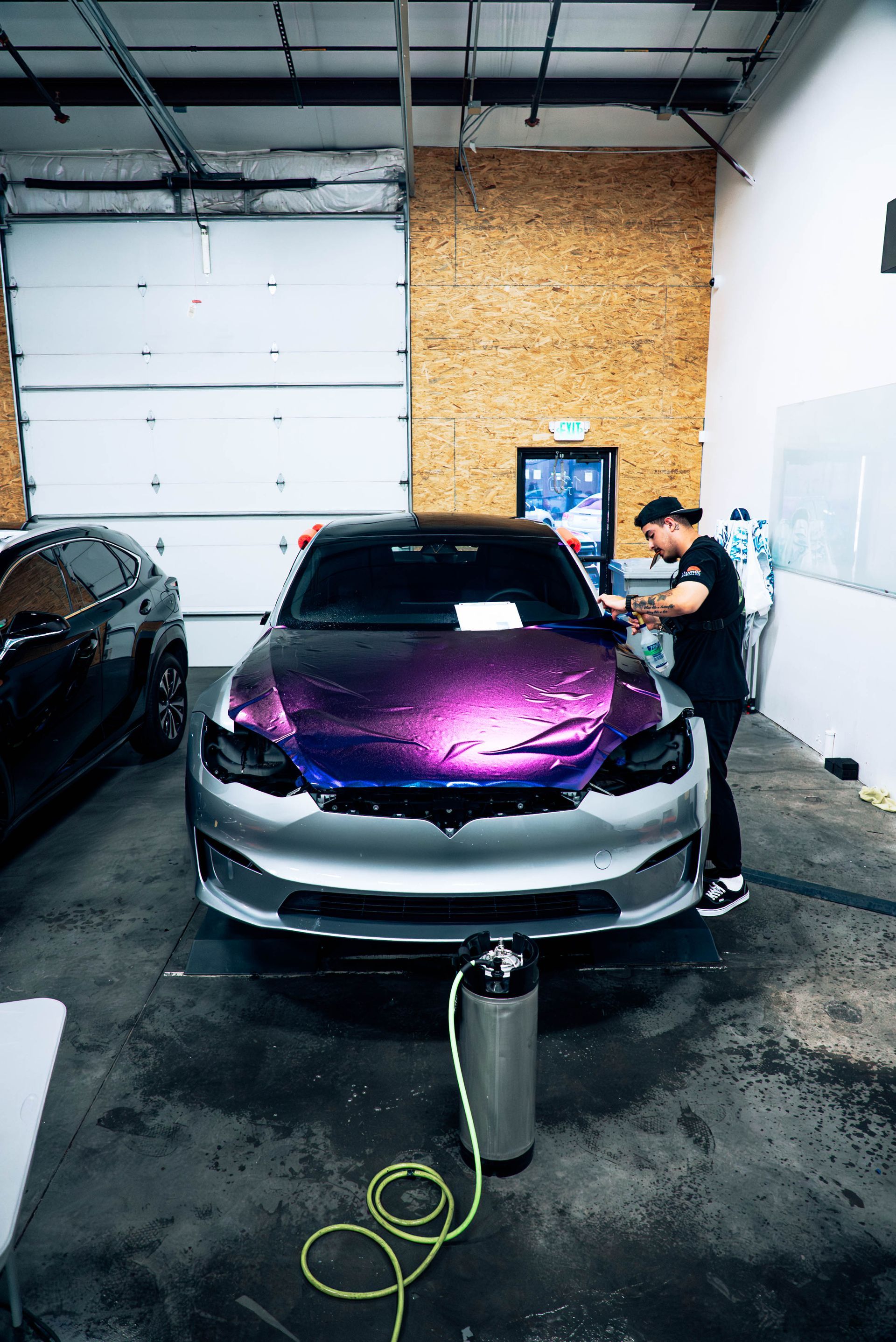 Purple car in a garage being washed by two people with a pressure washer