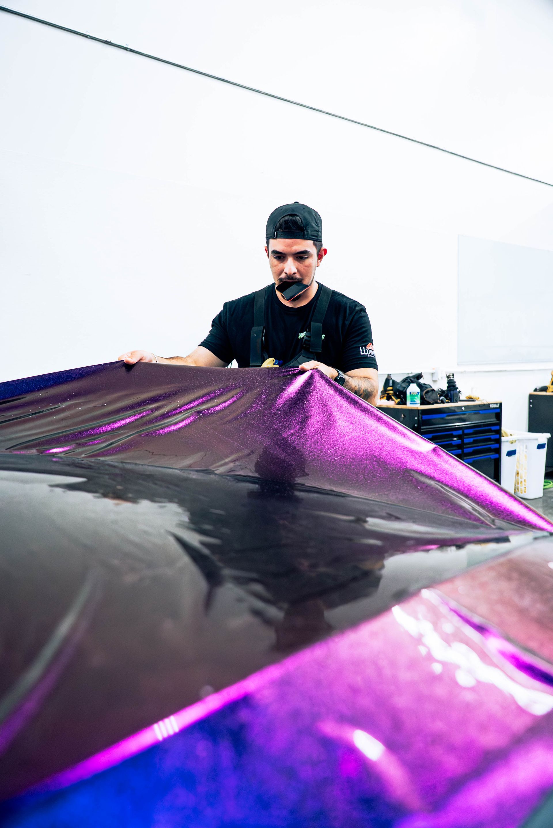 Person smoothing glossy purple film over a car in a workshop