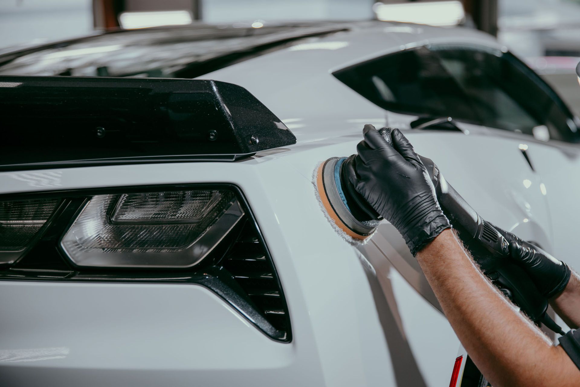 Gloved hands polish a white sports car’s rear panel in a garage