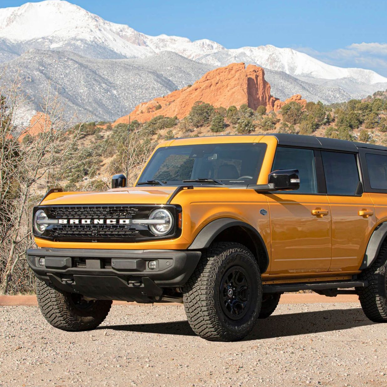 Yellow Ford Bronco SUV parked on dirt road, with mountains in the background.