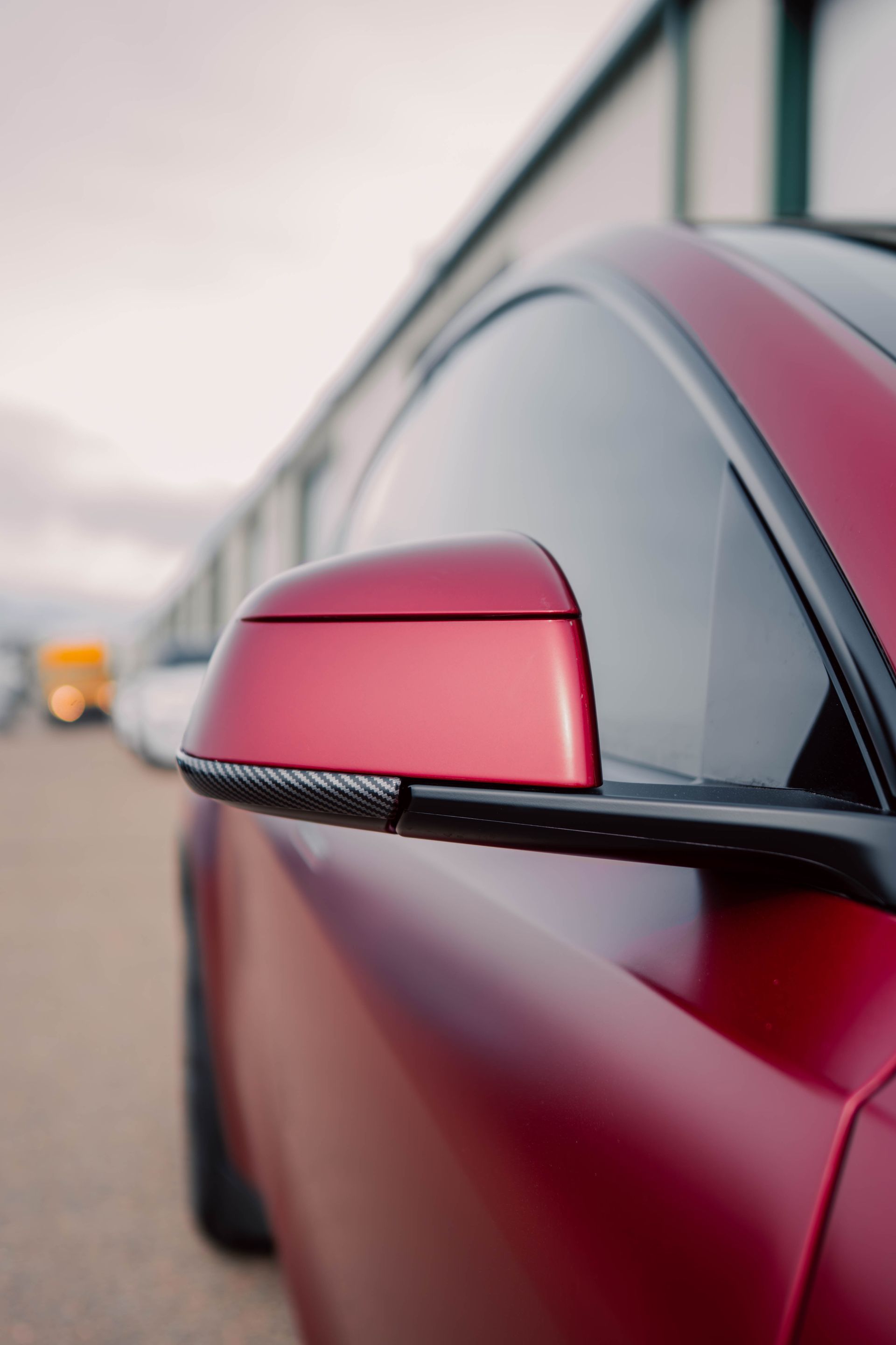 Close-up of a red car’s side mirror on a blurred roadside background