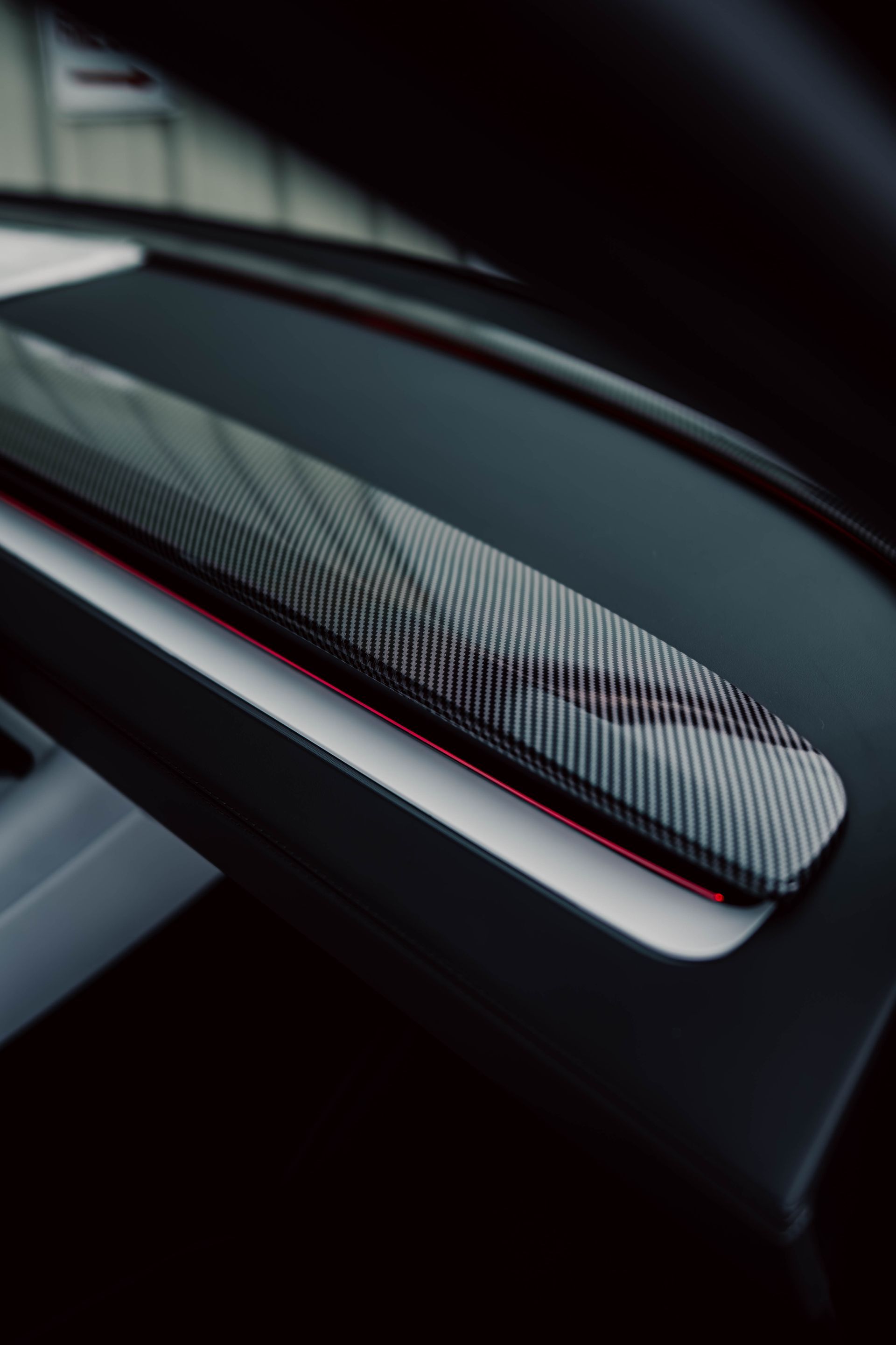 Close-up of a sleek black carbon-fiber car part with red trim in low light
