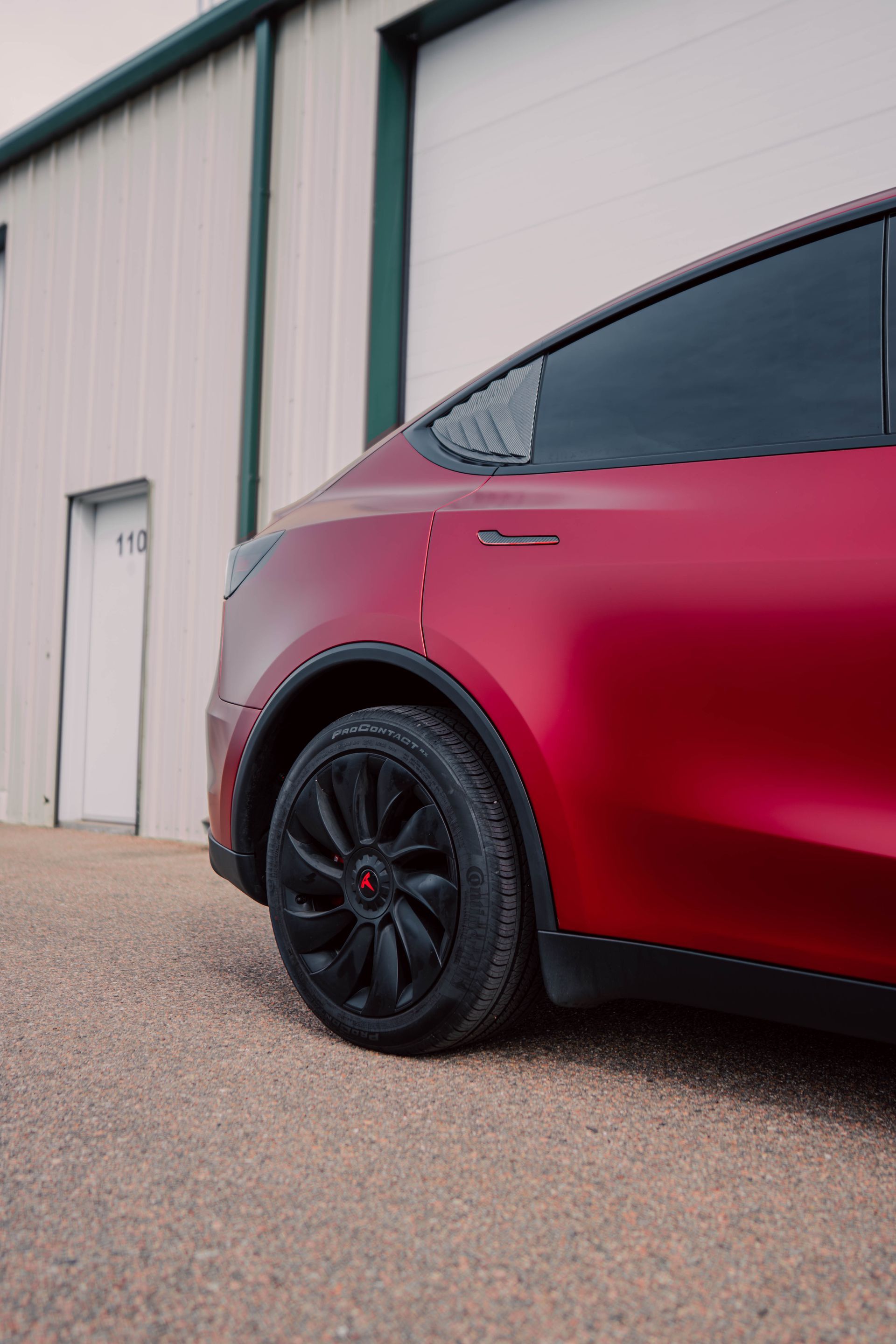 Red Tesla SUV parked beside an industrial building, showing the rear side and black wheel