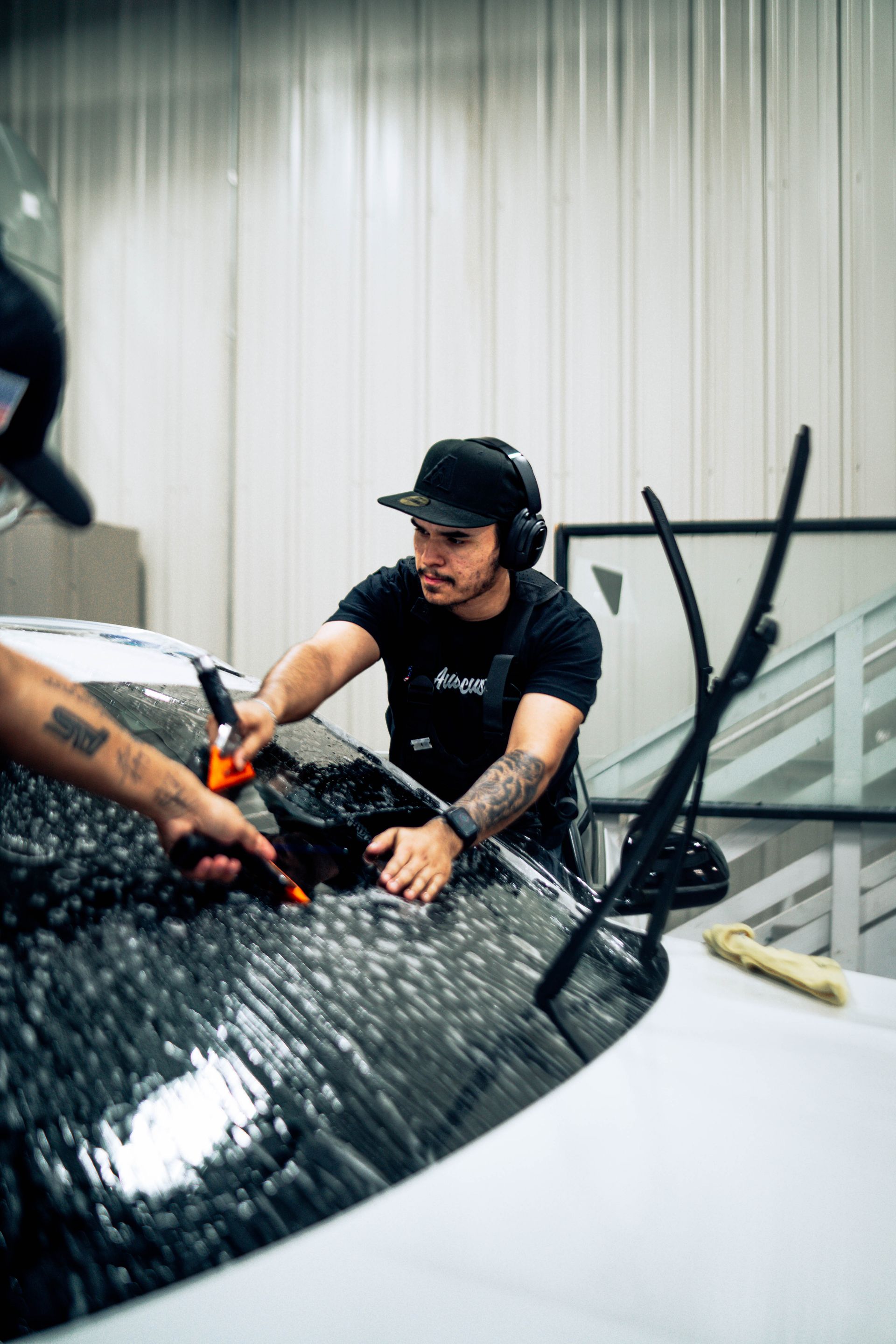 Man in black cap working on a glossy black car in a bright auto shop
