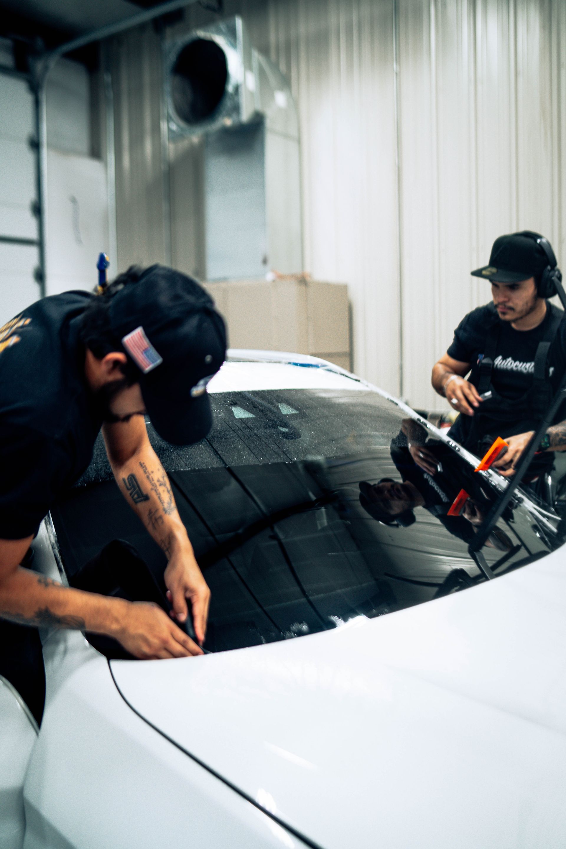 Two workers applying window tint to a white car in a garage