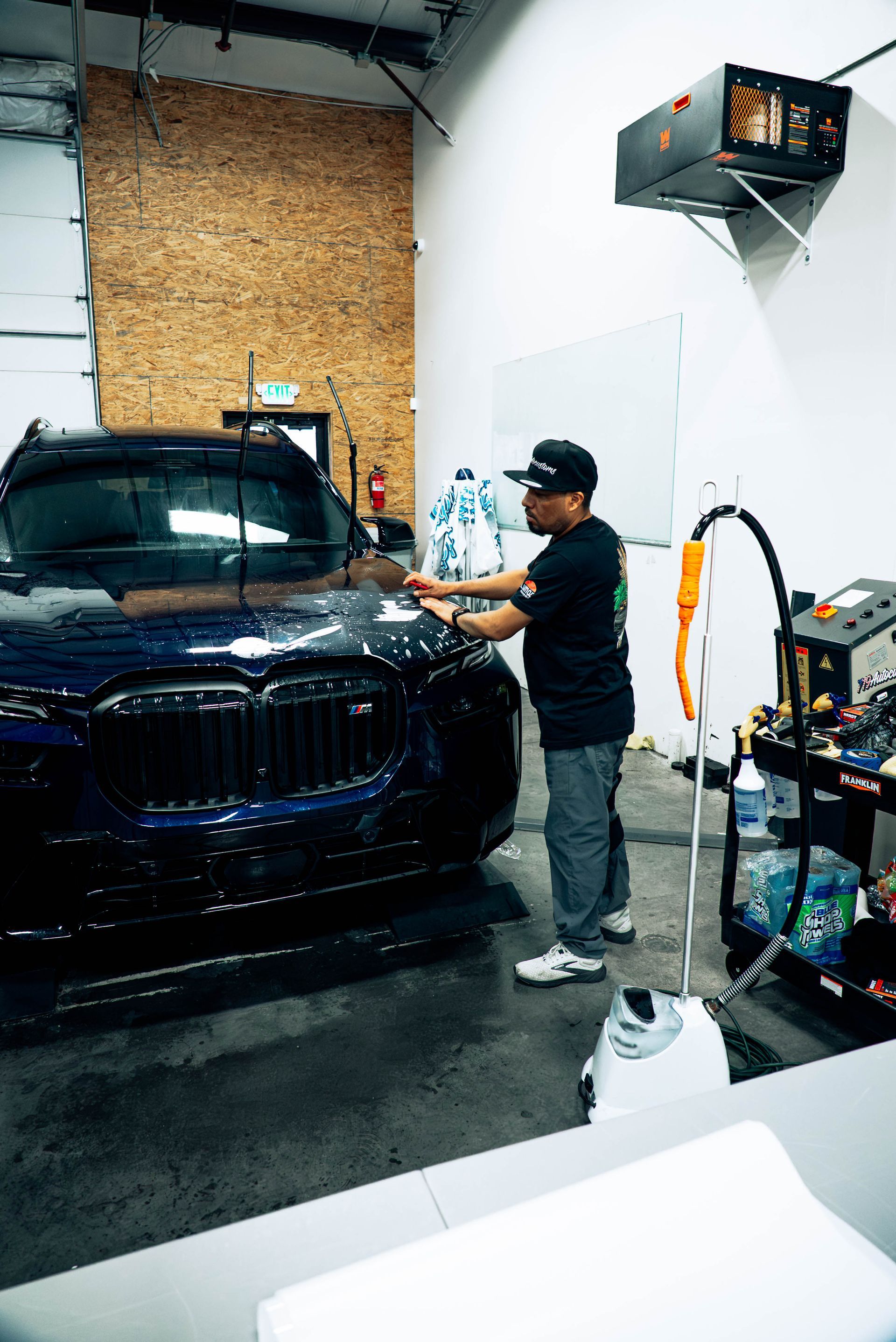Person detailing a black SUV in a garage, with cleaning tools and supplies nearby.