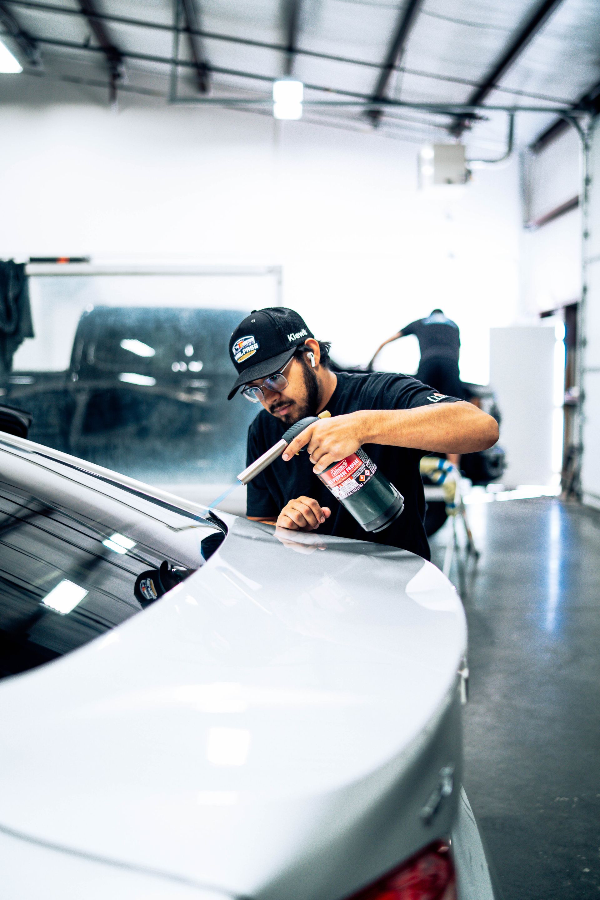 Person polishing a white car in an auto shop with a buffer tool